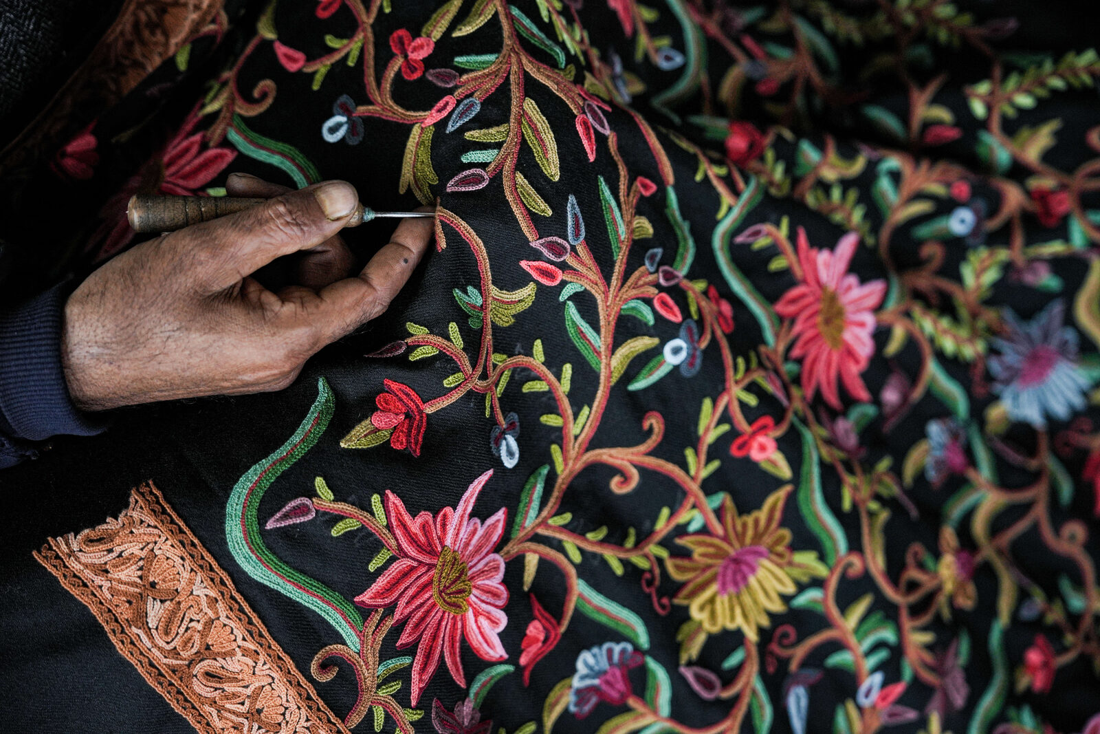 Artisan hand-working Aari hook embroidery in coloured thread on black fabric